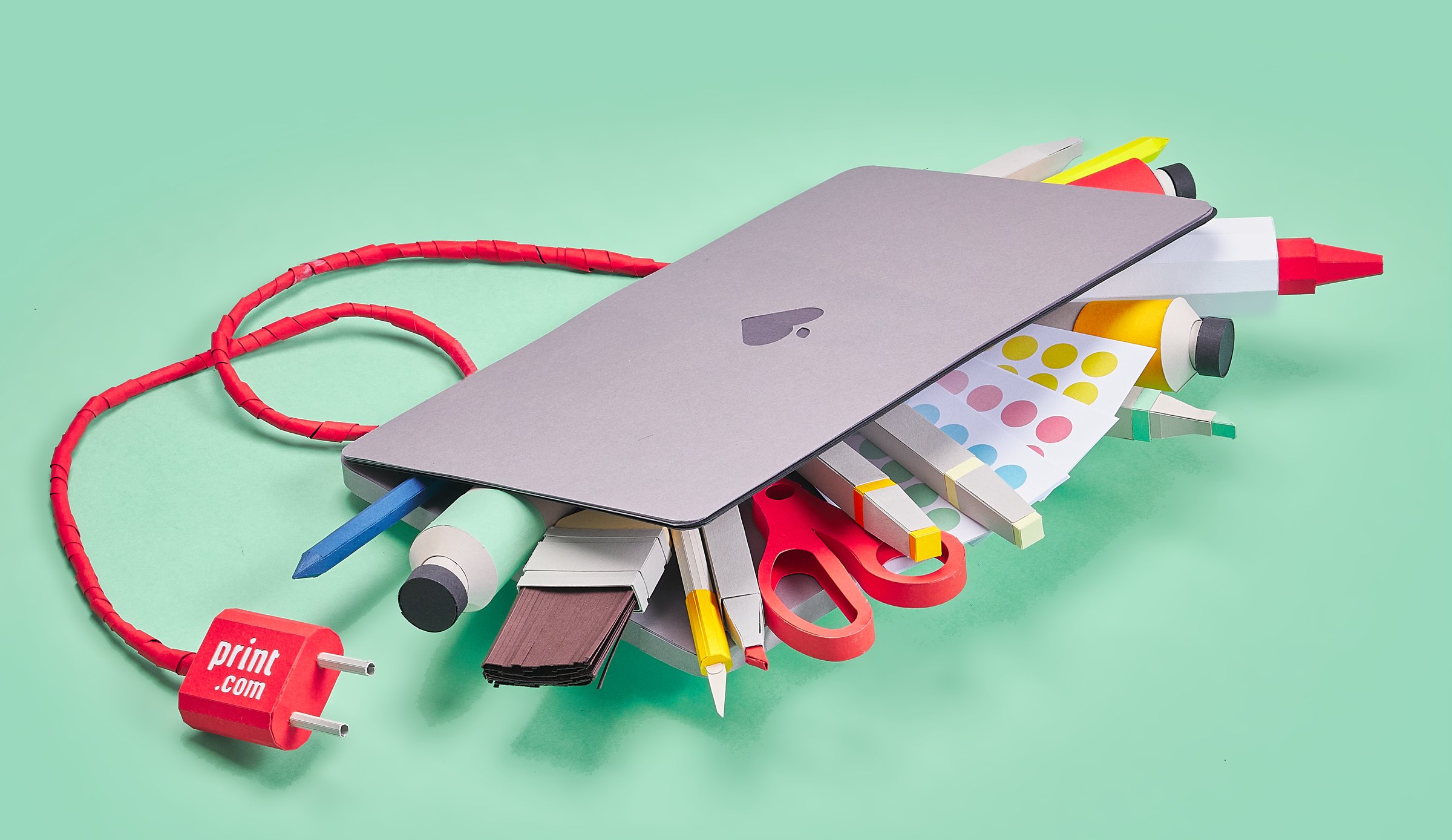 Laptop van papier vol creatieve materialen met een Print.com-stekker